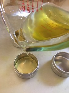 Pouring hot melted infused oils into tins.